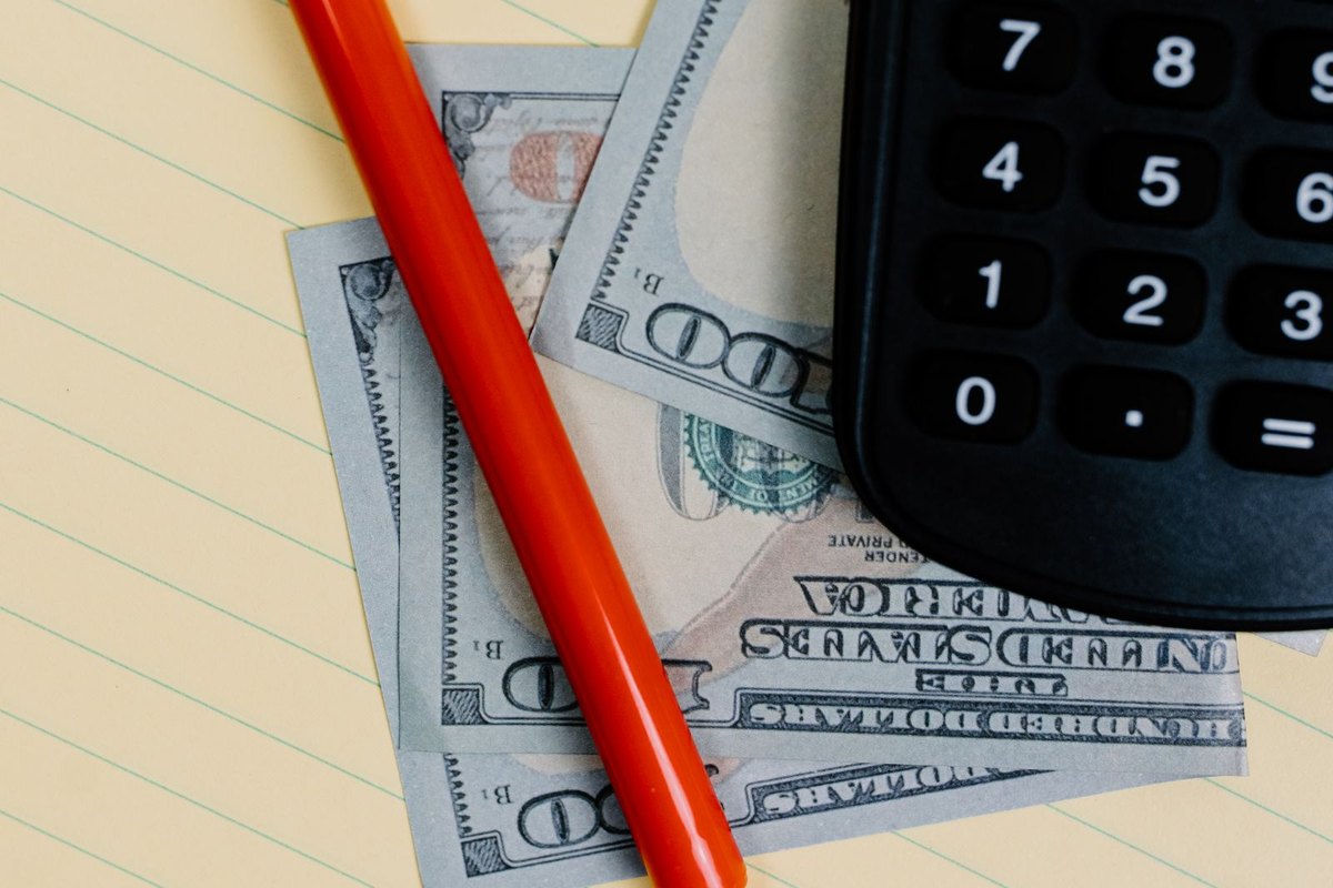 A calculator, cash and a pen on a yellow notepad