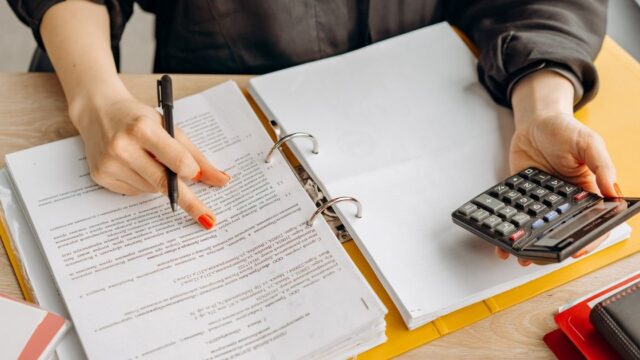 A woman reviewing documents with a calculator at a wooden table