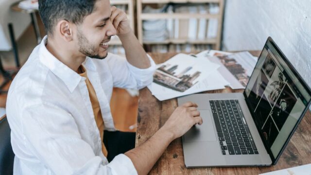 A man smiling as he works on a laptop at home