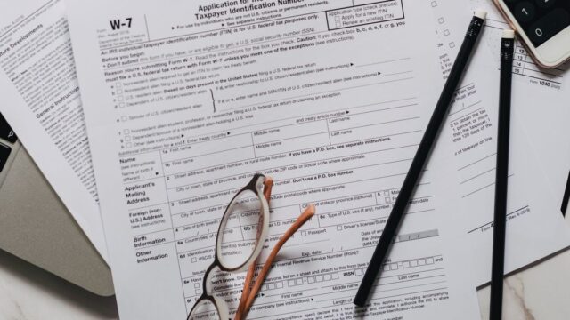 A pen and reading glasses lying on a blank tax form with a calculator