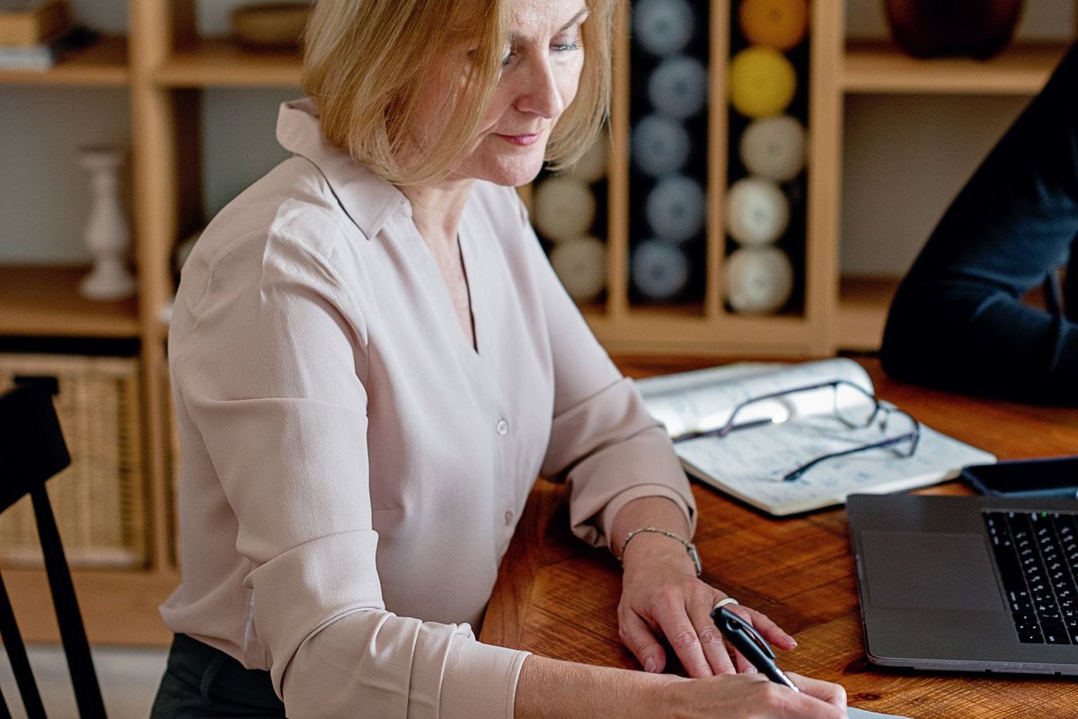 A woman writing notes at a wooden desk in her home office