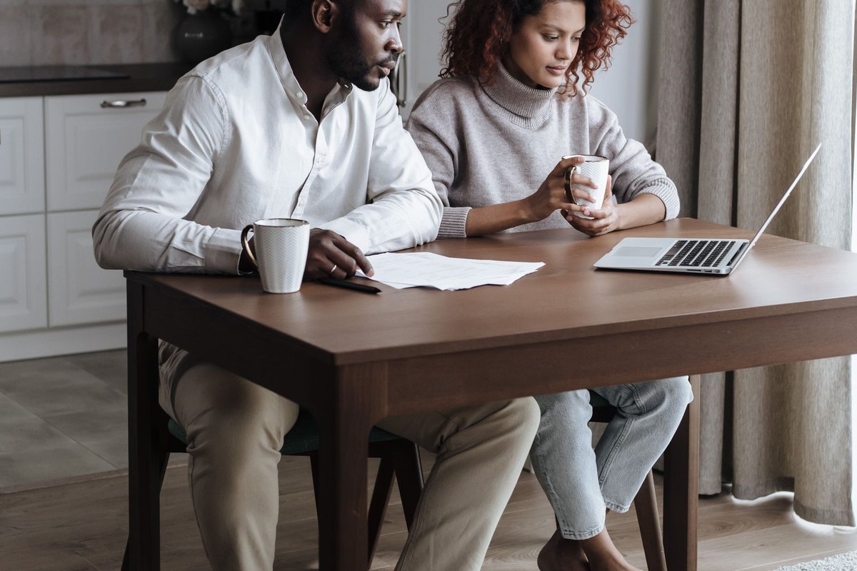 A couple at a kitchen table looking at a laptop together