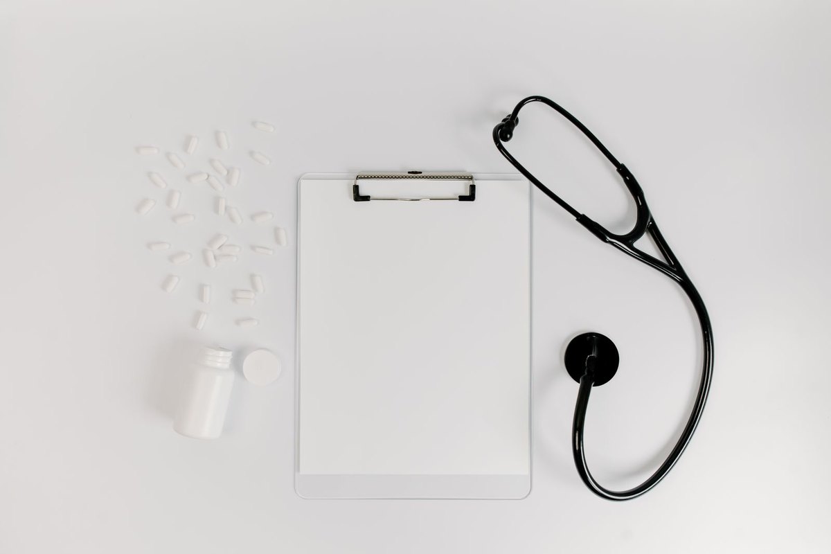 A clipboard with a form, a stethoscope and pills laid flat on a table