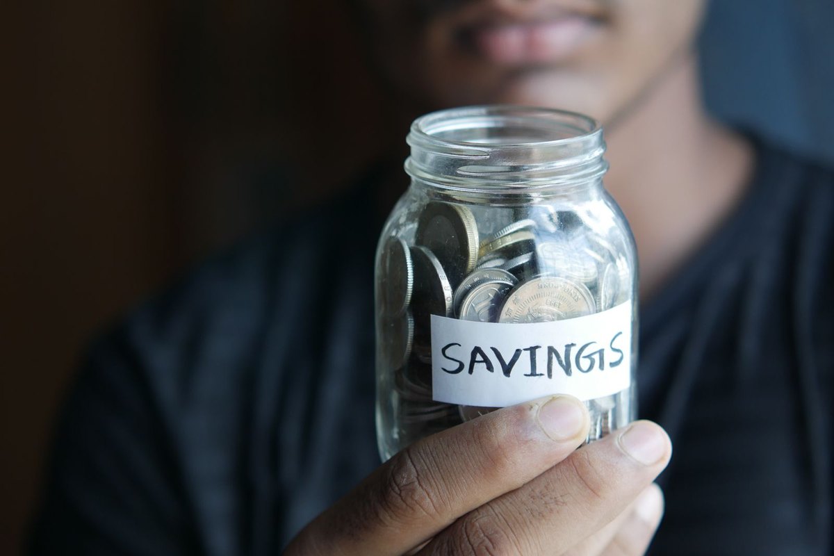 A hand holding a jar of coins labelled Savings