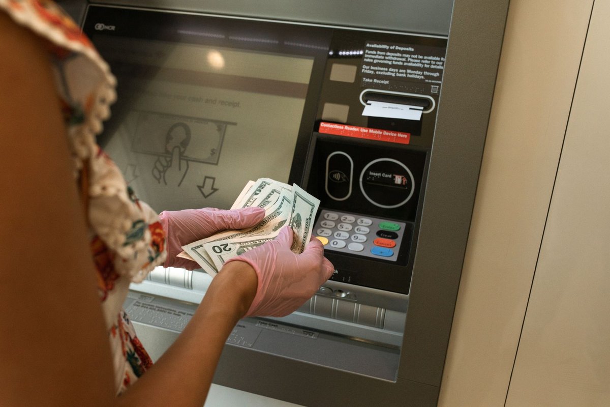 A person wearing gloves taking cash out of an ATM