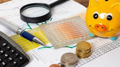 A desk with coins, a calculator, a pen, a financial sheet and a yellow piggy bank