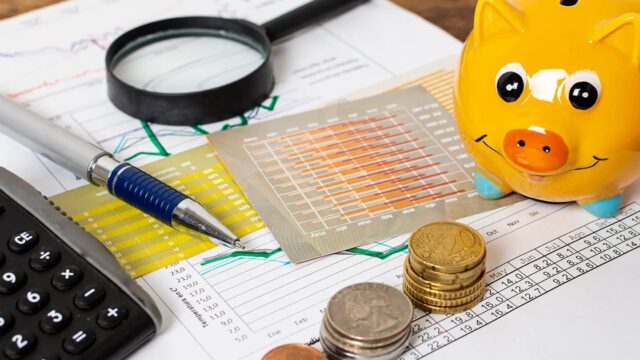 A desk with coins, a calculator, a pen, a financial sheet and a yellow piggy bank