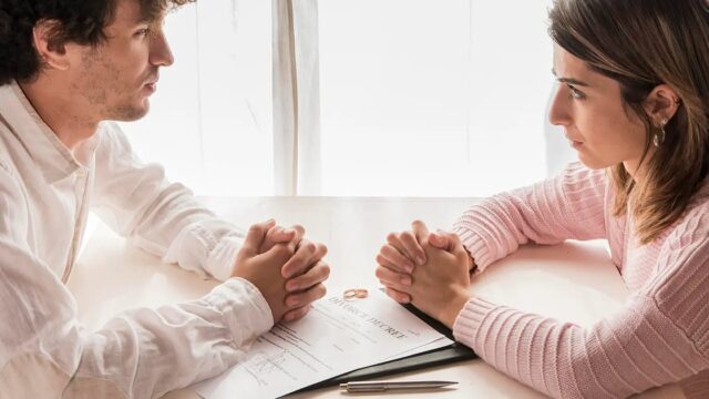 A man and a woman sitting across a table from each other holding hands over a document
