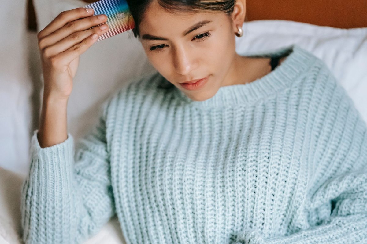 A woman sitting on her bed with a laptop and a credit card