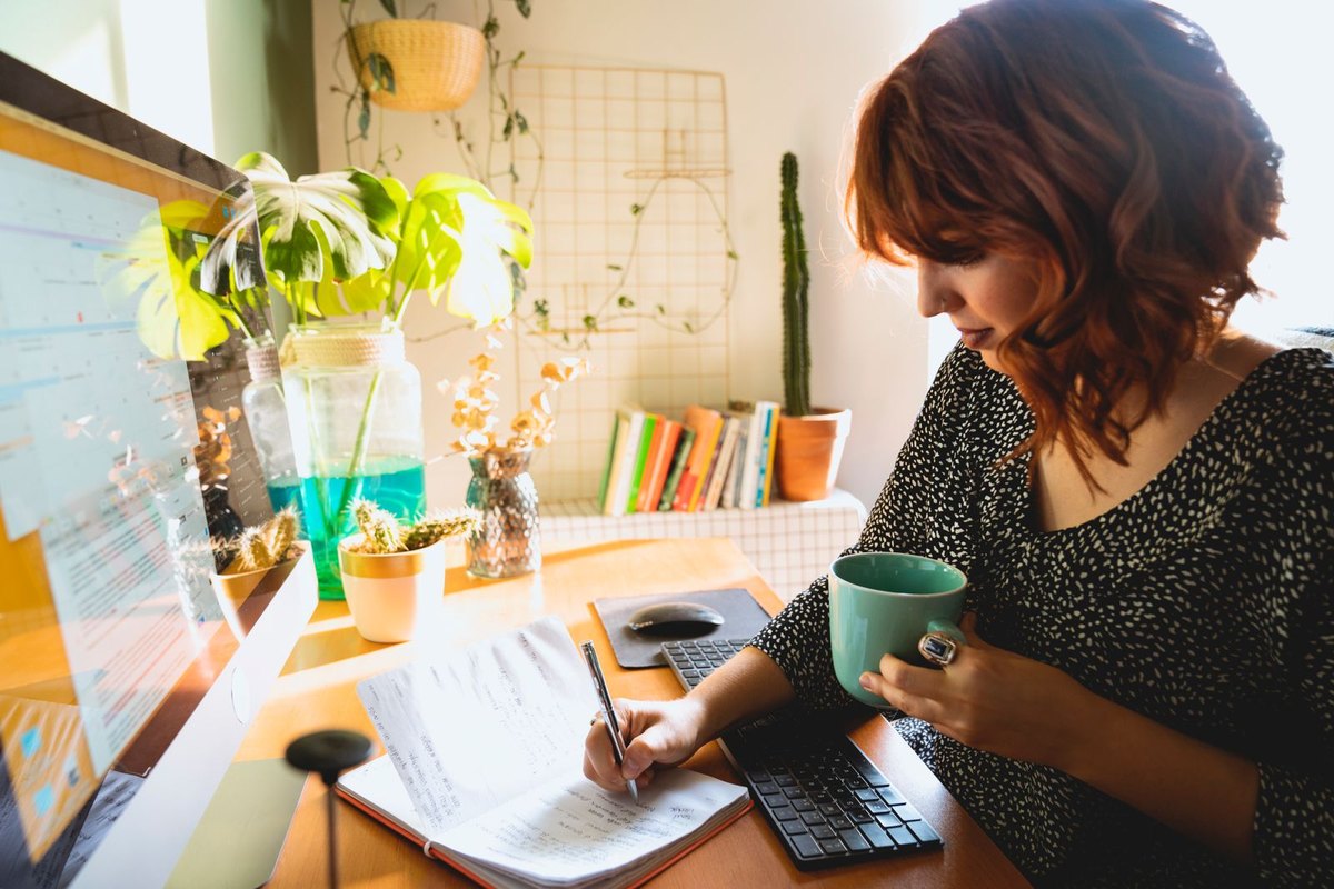 A woman writing in a notebook with a coffee cup at a sunny desk