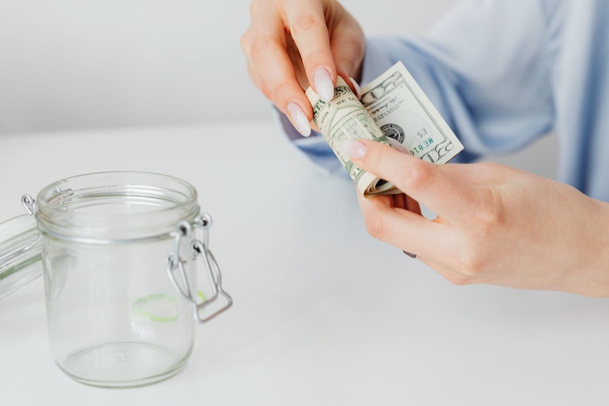 A woman rolling up dollar bills next to a glass jar