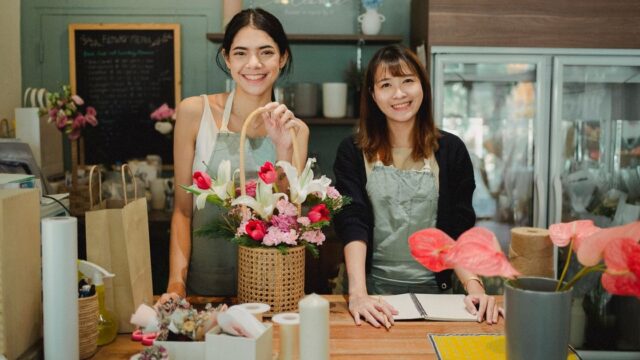 Two florists smiling behind the counter of their flower shop