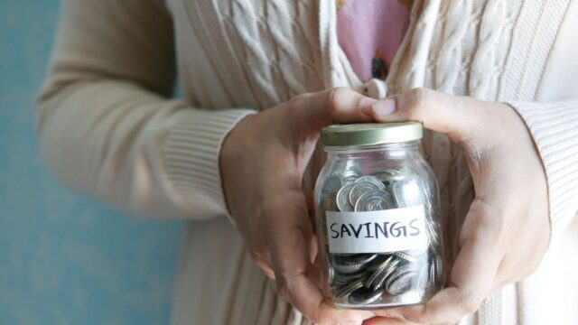 A woman holding a jar of coins labelled savings