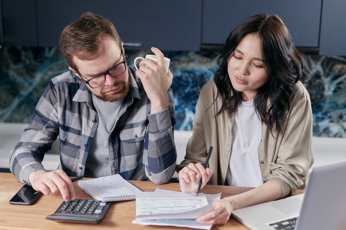 A couple going through household bills at their kitchen table with a calculator and laptop