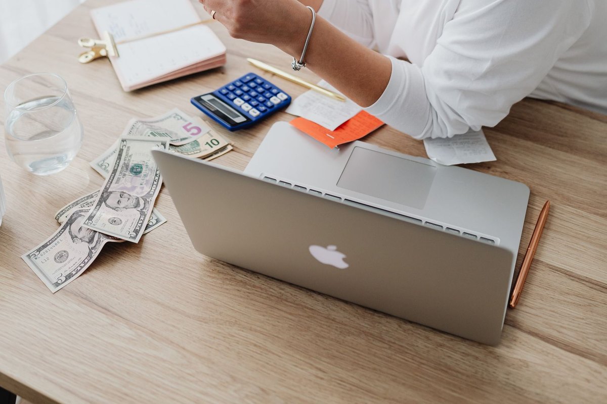 A woman at a desk with a laptop, cash and receipts working out a budget