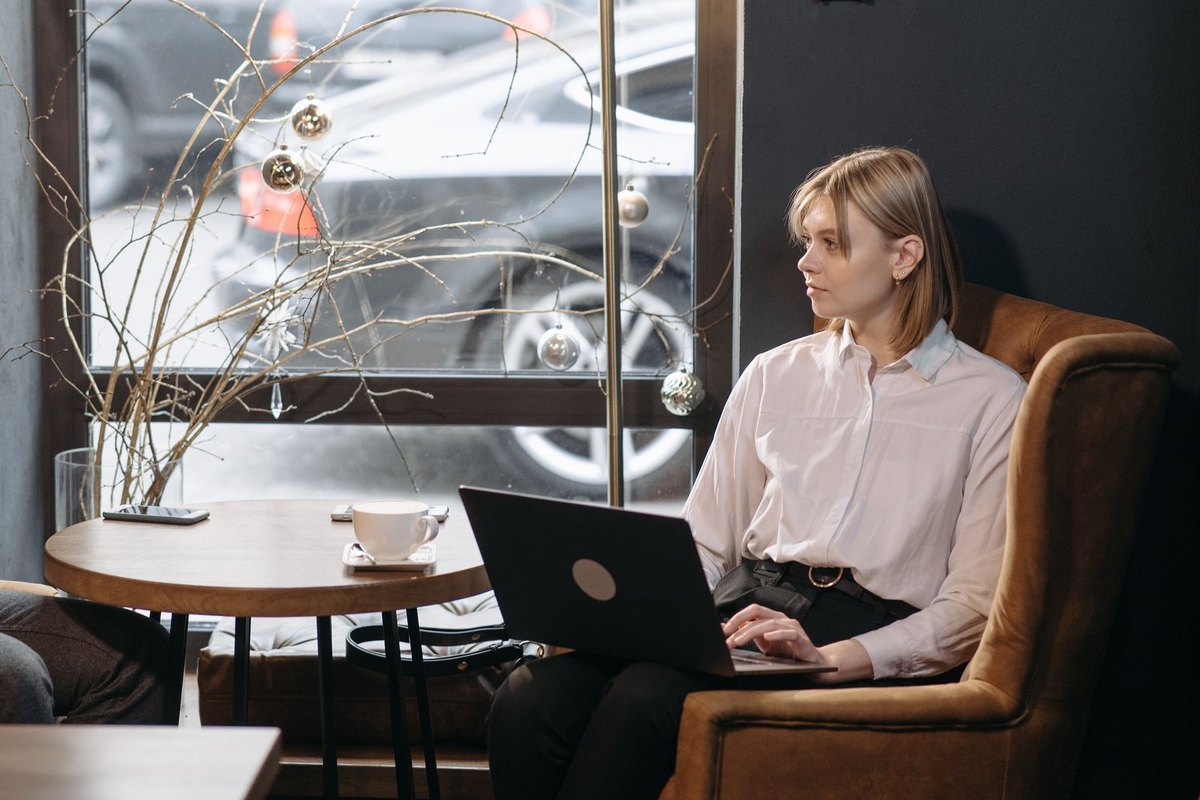 A woman working on a laptop at a café table by a window