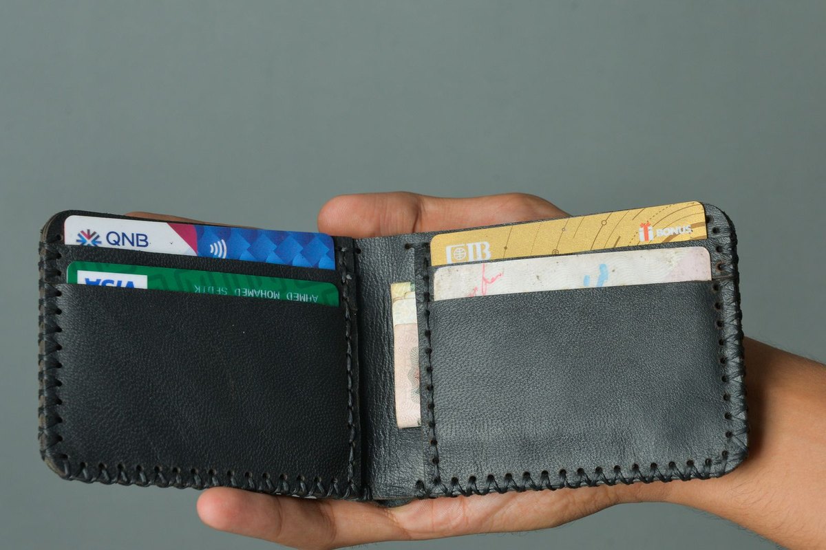 A hand holding an open leather wallet with cards inside