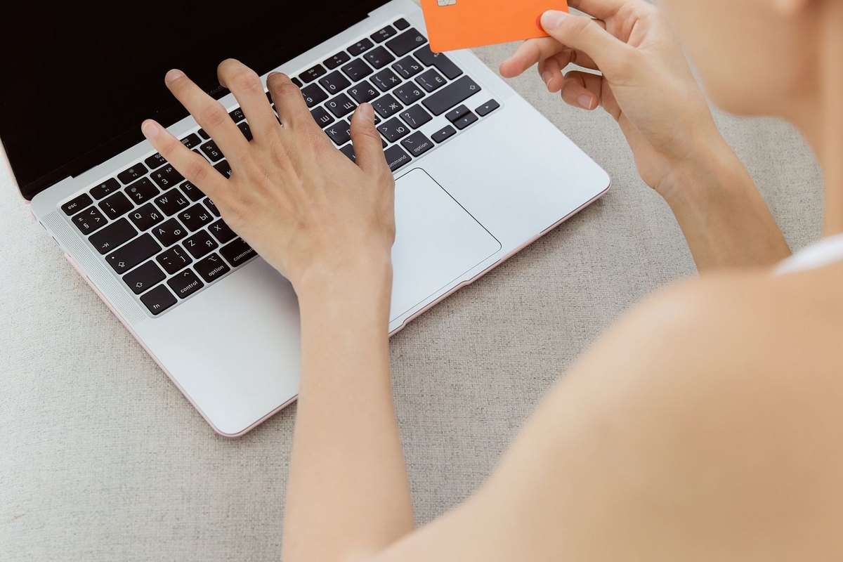 A woman holding a bank card while typing on a laptop
