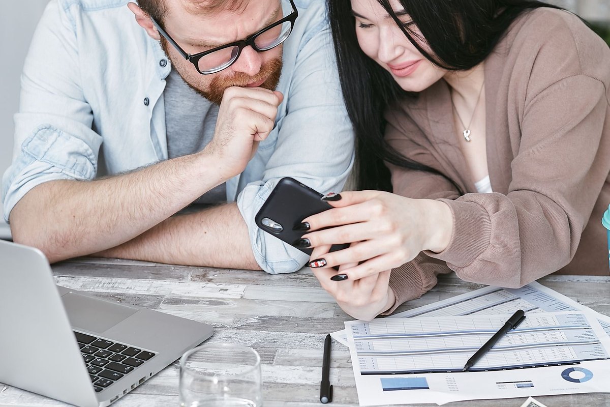 A man and woman looking at a smartphone and papers at a kitchen table