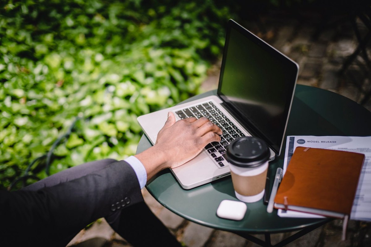 A freelancer working on a laptop at an outdoor café table with a coffee and papers