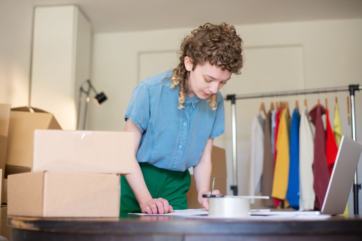 A woman packing orders at home next to a laptop and cardboard boxes